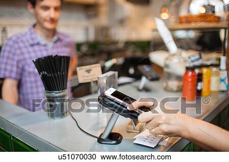 Stock Image - Cropped shot of female customer using smartphone contactless payment in cafe. Fotosearch