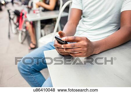 Cropped shot of young man texting on smartphone at city sidewalk cafe View Large Photo Image Stock Photo - Cropped shot of young man texting on smartphone at city sidewalk cafe. Fotosearch