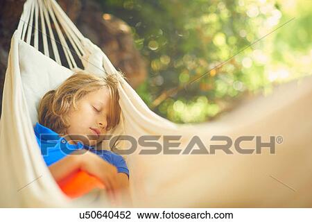 Stock Image - Cute boy reclining in garden hammock asleep. Fotosearch