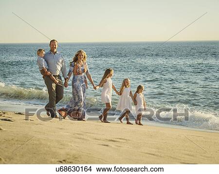 Picture - Family with children (12-17 months, 4-5, 6-7, 8-9) walking on beach with sea in background. Fotosearch