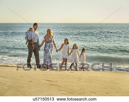 Stock Image - Family with children (12-17 months, 4-5, 6-7, 8-9) walking on beach with sea in background. Fotosearch