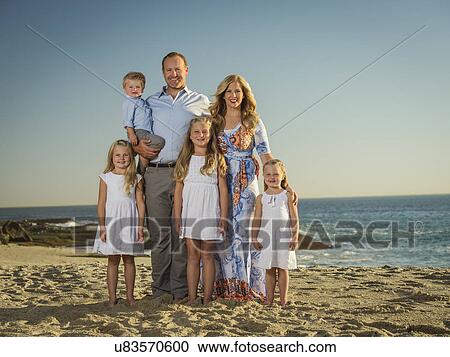 Stock Image - Family with children (12-17 months, 4-5, 6-7, 8-9) standing on beach with sea in background. Fotosearch