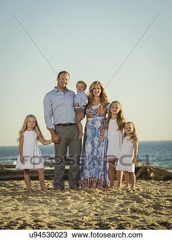 Stock Image - Family with children (12-17 months, 4-5, 6-7, 8-9) standing on beach with sea in background. Fotosearch