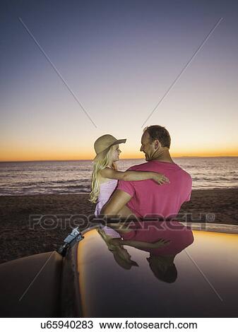 Stock Image - Father carrying daughter (4-5) next to car on beach. Fotosearch