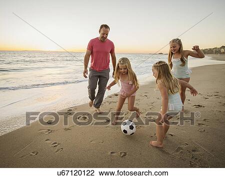 Stock Image - Father with children (4-5, 6-7, 8-9) playing soccer on beach. Fotosearch