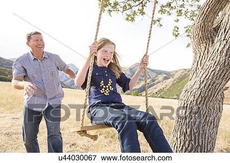 Stock Photo - Father with daughter (8-9) sitting on swing. Fotosearch