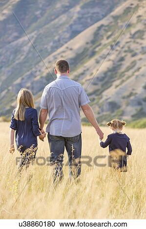 Stock Image - Father with two daughters (4-5, 8-9) walking in field. Fotosearch