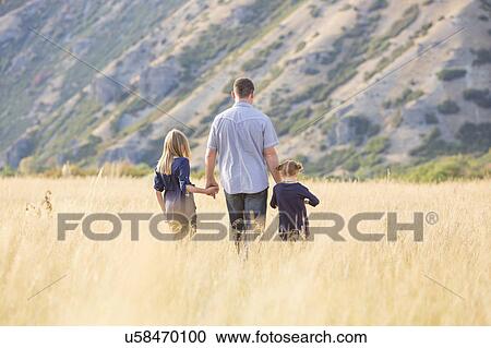 Stock Image - Father with two daughters (4-5, 8-9) walking in field. Fotosearch