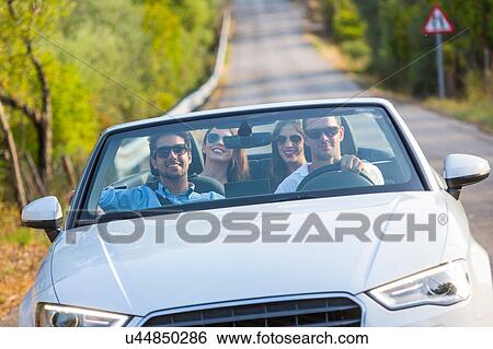 Stock Photograph - Four adult friends driving on rural road in convertible, Majorca, Spain. Fotosearch