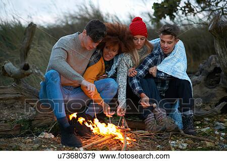 Four adult friends huddled together toasting marshmallows on beach at dusk View Large Photo Image Stock Photo - Four adult friends huddled together toasting marshmallows on beach at dusk. Fotosearch