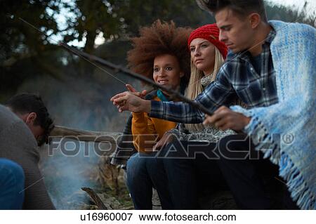 Stock Photo - Four adult friends igniting driftwood campfire on beach at dusk. Fotosearch