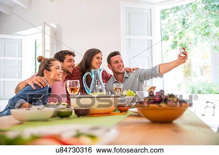 Stock Photograph - Friends dining together, taking a selfie. Fotosearch