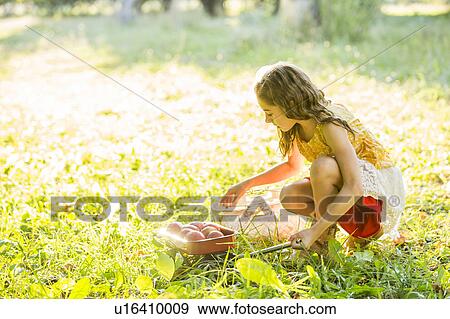 Stock Photo - Girl with fruit crouching in grass. Fotosearch