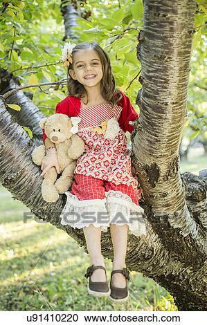 Stock Image - Girl with teddy bear sitting on tree. Fotosearch