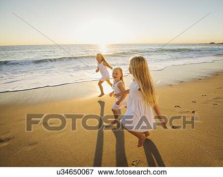 Stock Photo - Girls (4-5, 6-7, 8-9) running on beach. Fotosearch