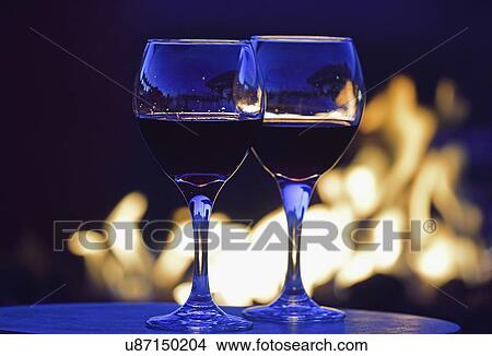 Picture - Glasses of red wine against fire pit at night. Fotosearch