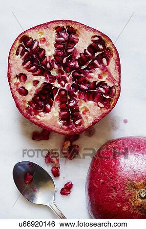 Stock Photograph - Halved Pomegranate and spoon against white background. Fotosearch