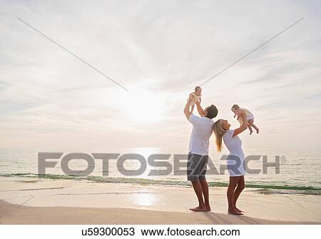 Stock Image - Happy family with two baby girls (2-5 months) at beach in sunlight. Fotosearch