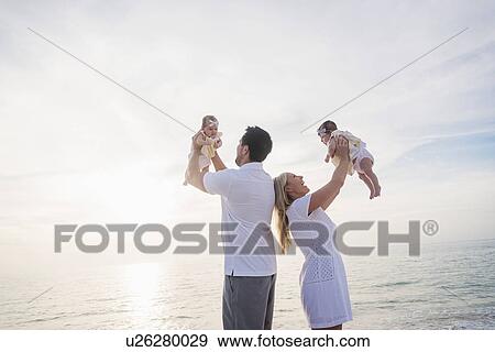 Stock Photo - Happy family with two baby girls (2-5 months) at beach in sunlight. Fotosearch