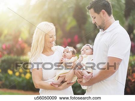 Stock Photo - Happy family with two baby girls (2-5 months) at park. Fotosearch