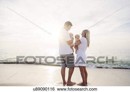 Stock Photograph - Happy family with two baby girls (2-5 months) at beach in sunlight. Fotosearch