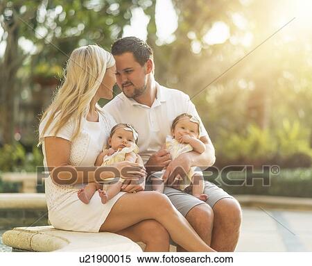 Stock Photography - Happy family with two baby girls (2-5 months) at park in sunlight. Fotosearch