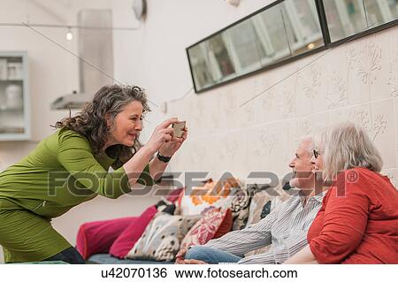 Stock Photograph - Happy seniors taking photograph on couch. Fotosearch