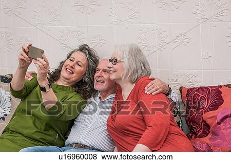 Stock Photo - Happy seniors taking selfie on couch. Fotosearch