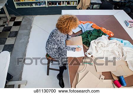 High angle view of mature female fashion designer drawing in sketchbook at workshop table View Large Photo Image Stock Image - High angle view of mature female fashion designer drawing in sketchbook at workshop table. Fotosearch