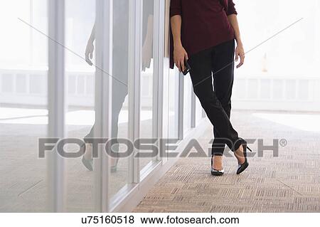 Stock Photo - Low section of young woman leaning on glass wall. Fotosearch
