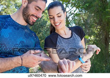 Stock Image - Male and female runners checking smartwatches in park, Split, Dalmatia, Croatia. Fotosearch