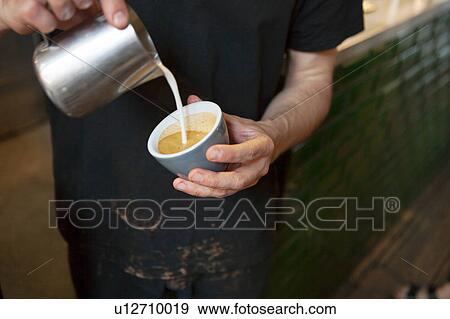 Stock Photo - Male barista's hands pouring milk into coffee cup in cafe. Fotosearch