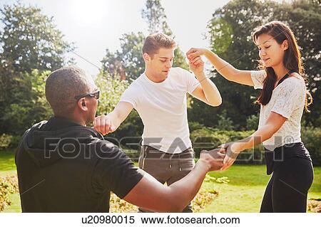 Stock Photography - Man and woman holding hands with personal trainer balancing in park. Fotosearch