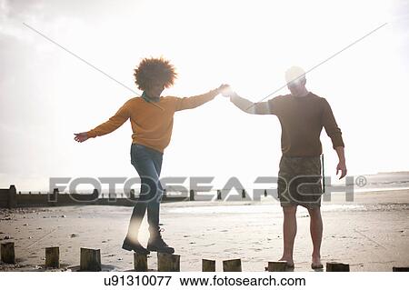 Man helping woman balance on wooden stumps on beach View Large Photo Image Stock Photo - Man helping woman balance on wooden stumps on beach. Fotosearch