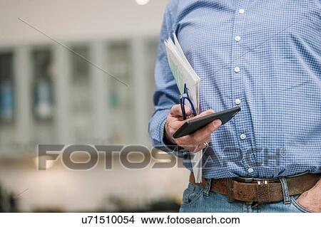 Man holding mobile phone, reading glasses, with book under arm View Large Photo Image Picture - Man holding mobile phone, reading glasses, with book under arm. Fotosearch