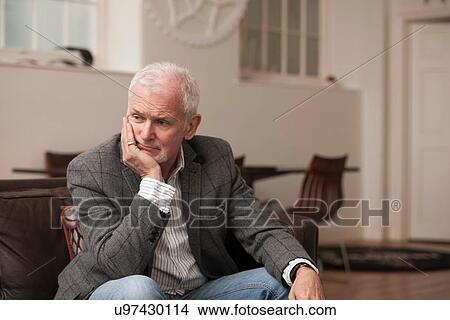 Picture - Man looking upset on couch. Fotosearch