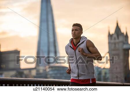 Picture - Man running by riverside, Tower Bridge and The Shard in background, Wapping, London, UK. Fotosearch