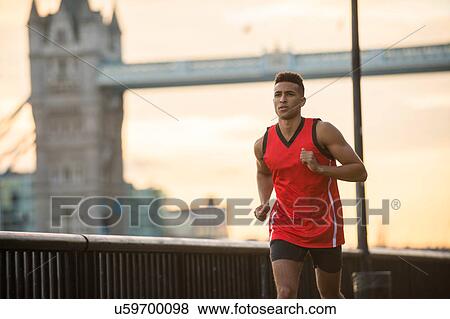 Stock Photo - Man running by riverside, Tower Bridge in background, Wapping, London, UK. Fotosearch
