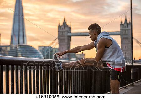 Stock Photography - Man stretching against railing, Tower Bridge and The Shard in background, Wapping, London, UK. Fotosearch