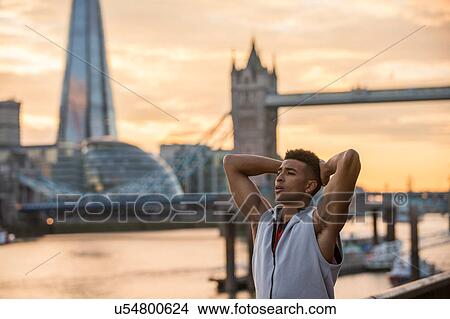 Picture - Man stretching by riverside, Tower Bridge and The Shard in background, Wapping, London, UK. Fotosearch