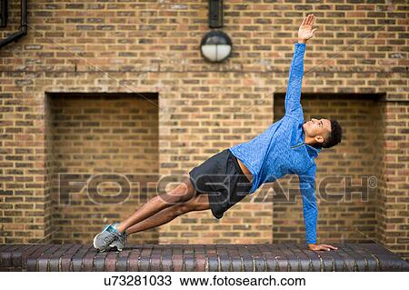 Stock Image - Man stretching in front of brick wall, Wapping, London, UK. Fotosearch