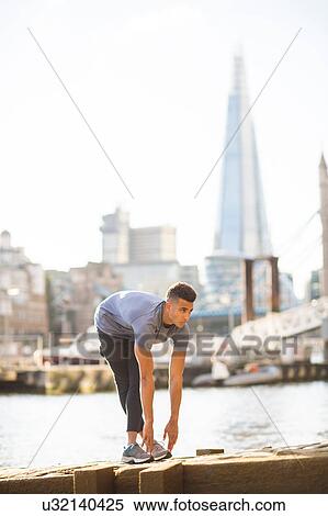 Stock Photography - Man stretching on pier, The Shard in background, Wapping, London, UK. Fotosearch