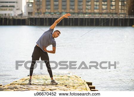 Stock Image - Man stretching on pier, Wapping, London, UK. Fotosearch