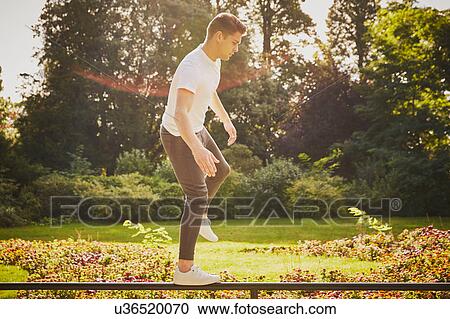 Stock Image - Man training, balancing on one leg on park fence. Fotosearch