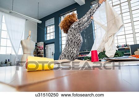 Mature female fashion designer holding up textile by workshop table View Large Photo Image Stock Image - Mature female fashion designer holding up textile by workshop table. Fotosearch