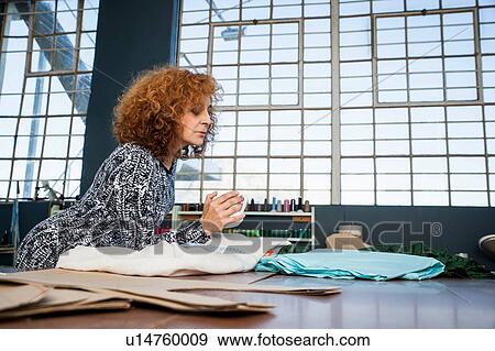 Mature female fashion designer leaning on workshop table looking at textiles View Large Photo Image Stock Photo - Mature female fashion designer leaning on workshop table looking at textiles. Fotosearch