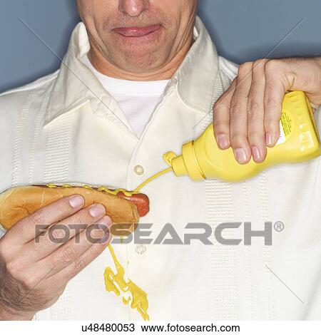 Stock Image - Mature man holding hotdog and accidentally spilling mustard on shirt. Fotosearch
