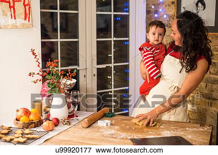 Stock Photo - Mature woman preparing Christmas cookies with baby son at kitchen counter. Fotosearch