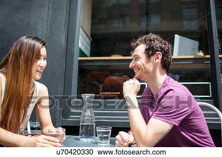 Stock Image - Mid adult couple chatting at city sidewalk cafe. Fotosearch