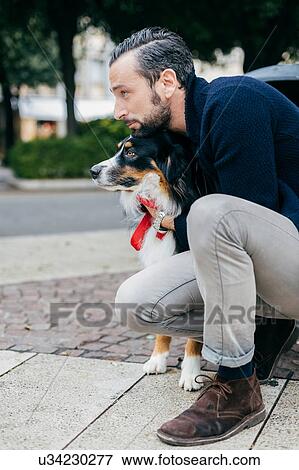 Stock Photo - Mid adult man crouching with pet dog on city sidewalk. Fotosearch